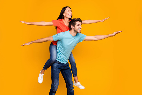 Profile photo of funny guy carry lady piggyback spend summer together spread hands like wings wear casual stylish blue orange t-shirts jeans isolated yellow color background - Foto, Imagen