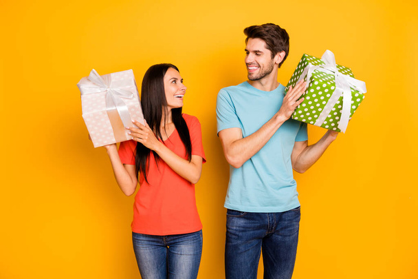 Photo of two funny guy lady people holding hands big giftboxes looking eyes thankful wear casual trendy blue orange t-shirts jeans isolated yellow color background - 写真・画像