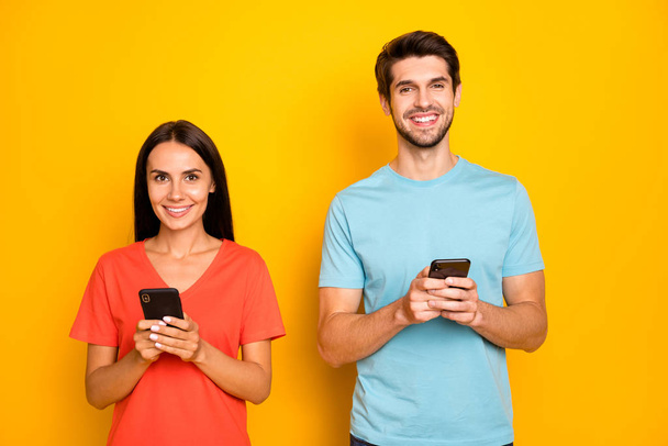 Photo of two funny guy lady people couple hold telephones arms reading social network post comments wear casual blue orange t-shirts isolated yellow color background - Φωτογραφία, εικόνα