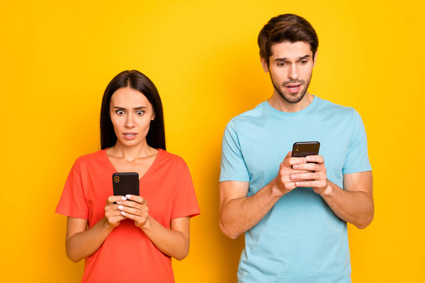 Photo of two guy lady people couple hold telephones hands reading negative post comments open mouth wear casual blue orange t-shirts isolated yellow color background - Fotó, kép