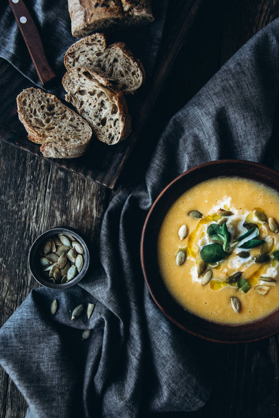 Pumpkin cream soup with cream and pumpkin seeds in a beautiful setting with pumpkin pieces, dark bread and leek on a dark background - Photo, Image