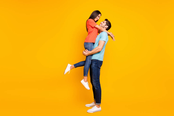 Full body photo of two cute people couple guy holding carrying lady look eyes lovely weekend romance moment wear casual blue orange t-shirts jeans isolated yellow color background - Foto, immagini