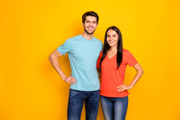 Photo of funny lovely two people couple guy and lady hugging hands by sides one best team wear casual blue orange t-shirts jeans isolated over yellow color background - Фото, изображение