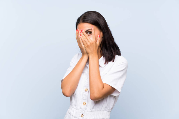 Mladá žena na izolovaném modrém pozadí zakrývající oči a procházející prsty - Fotografie, Obrázek
