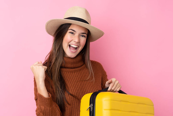 Девочка-подросток на изолированном розовом фоне в отпуске с чемоданом и шляпой - Фото, изображение