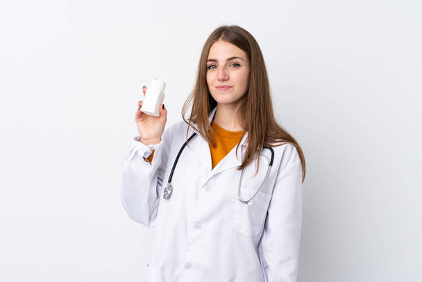 Νεαρή γυναίκα πάνω από απομονωμένη φόντο φορώντας ένα φόρεμα γιατρό και κρατώντας χάπια - Φωτογραφία, εικόνα