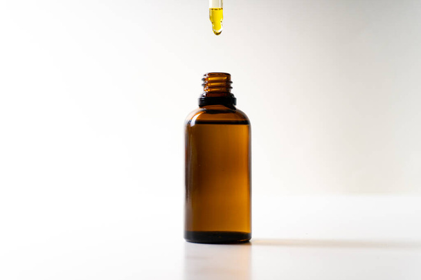 Aceite de CBD o cualquier otro aceite que cae en una botella pequeña - fondo blanco
 - Foto, Imagen
