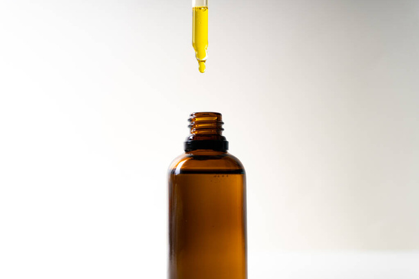 CBD oil or any other oil dropping into a small bottle - white background - close up - Photo, Image