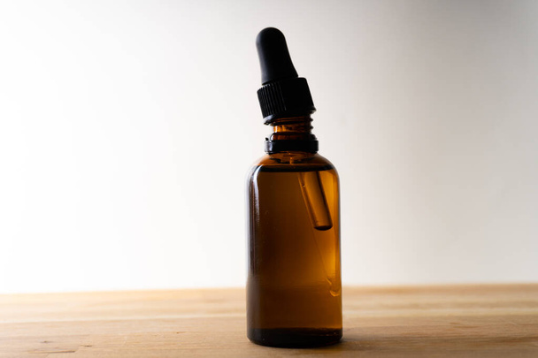 A small bottle with a dropper full of CBD oil or any other oil standing on a wooden board - white background - Valokuva, kuva