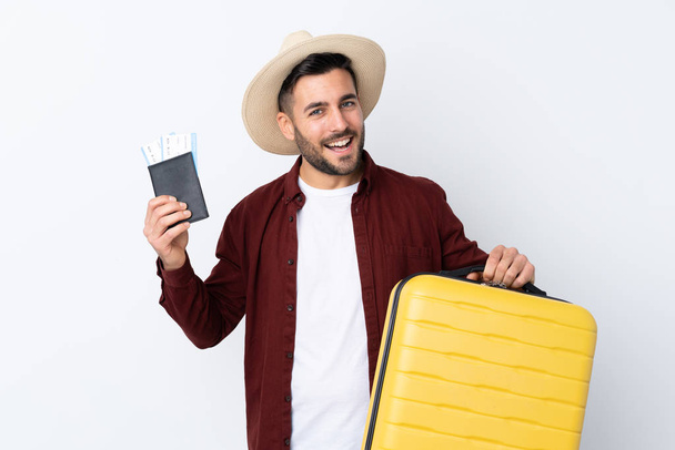 İzole edilmiş beyaz bir geçmişi olan genç yakışıklı bir adam, bavul ve pasaportla tatilde. - Fotoğraf, Görsel