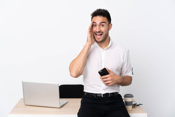 Young business man with a mobile phone in a workplace shouting with mouth wide open - Photo, image