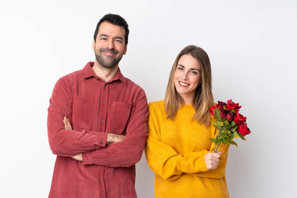 Ζευγάρι σε Ημέρα του Αγίου Βαλεντίνου κρατώντας λουλούδια πάνω από απομονωμένο φόντο κρατώντας τα χέρια σταυρωμένα σε μετωπική θέση - Φωτογραφία, εικόνα