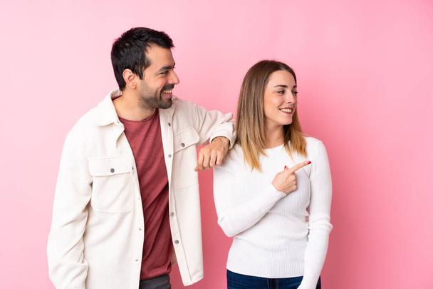 Couple en Saint Valentin sur fond rose isolé pointant vers le côté pour présenter un produit
 - Photo, image