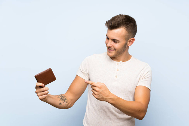 Young handsome blonde man over isolated blue background holding a wallet - Photo, Image