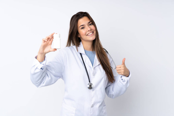 Teenager dívka přes izolované bílé pozadí nosí doktorské šaty a drží pilulky - Fotografie, Obrázek