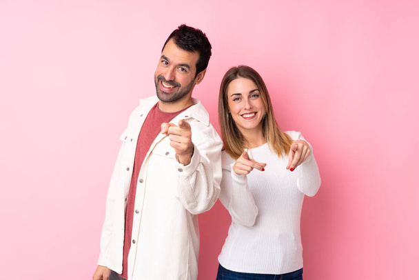 Paar in Valentijnsdag over geïsoleerde roze achtergrond wijst vinger naar je tijdens het glimlachen - Foto, afbeelding