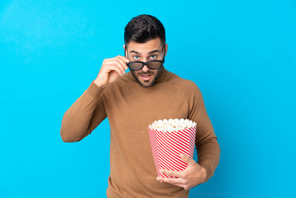 junger schöner Mann überrascht mit 3D-Brille und hält einen großen Eimer Popcorn in der Hand - Foto, Bild