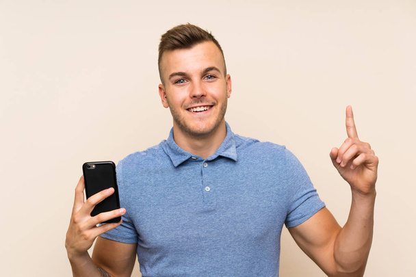 Mladý blondýnka muž pomocí mobilního telefonu ukazuje nahoru skvělý nápad - Fotografie, Obrázek