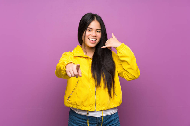 jong tiener aziatische meisje over geïsoleerde paarse achtergrond maken telefoon gebaar en wijzen front - Foto, afbeelding