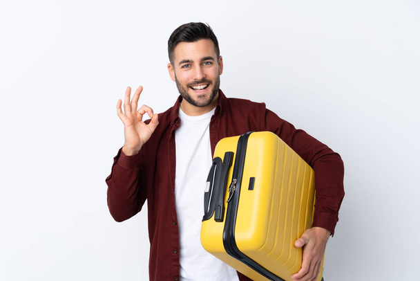 Jeune homme beau sur fond blanc isolé en vacances avec valise de voyage et faire signe OK
 - Photo, image