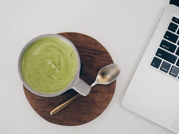 Top View notebook a keramický šálek veganského nápoje zelený čaj matcha latte na bílém stole - Fotografie, Obrázek