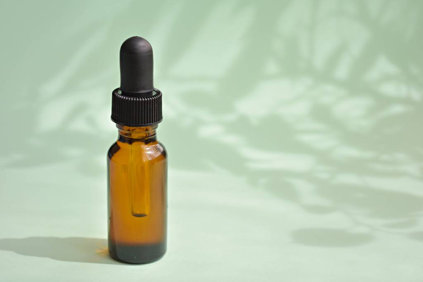 Aromaterapi, yağlı damlatıcı şişesi, cilt bakımı ürünü, kozmetik yağ şişesi maketi, ağaç yapraklı yeşil arka plan gölgeleri.. - Fotoğraf, Görsel