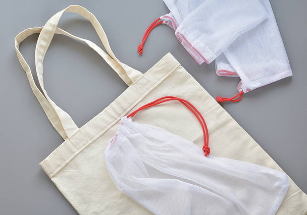 Handmade cotton grocery bag and reusable mesh produce bags on gray table, zero waste shopping, sustainable living - 写真・画像