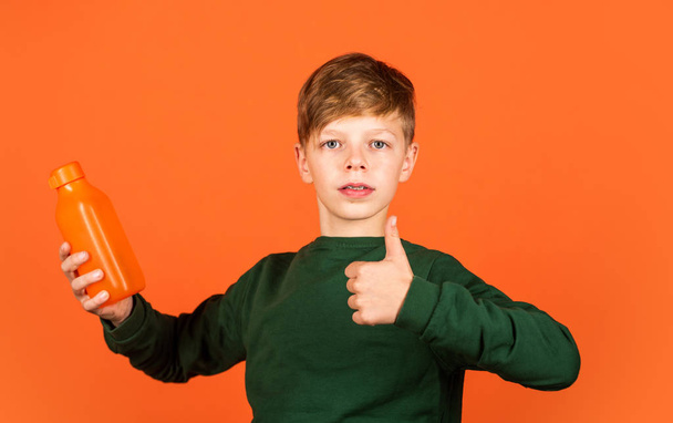 You will like this product. Small boy show thumbs up for juice orange background. Vitamin drink. Drinking product. Bottle with organic product. Healthy drinking habits. Promoting product - 写真・画像