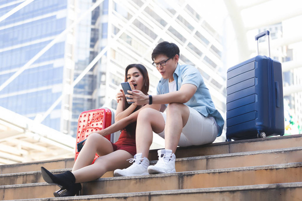 Jovem casal homem e mulher com bagagem olhando sorriso smartphone e feliz na cidade de negócios, conceito de viagem casal
. - Foto, Imagem
