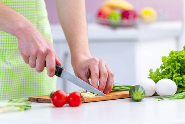 家庭のキッチンで新鮮な健康的な野菜サラダのためのエプロンチョッピングエコフレンドリーな製品で調理女性。食事ときれいな食べ物。野菜料理の準備 - 写真・画像