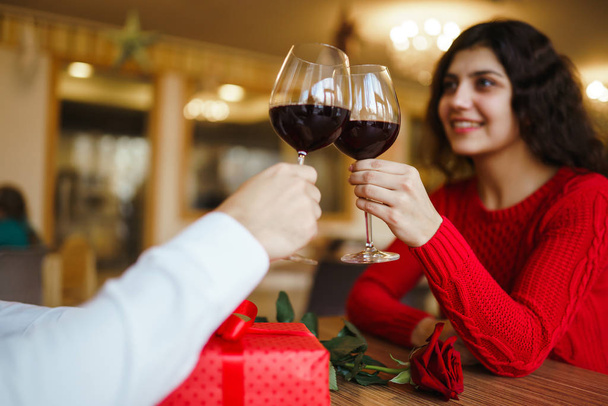 Young couple having a romantic dinner and toasting with cups of red wine. Sweet couple celebrate their anniversary. Valentines day celebration concept. Relationship, surprise and love concept. - Φωτογραφία, εικόνα