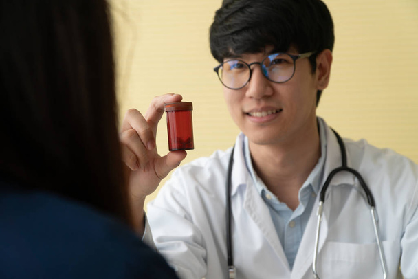 Азіатський лікар зі стетоскопом і уніфікованою формою, що містить пляшку для ліків і пояснює лікувальні властивості пацієнтів. Концепція медичного консультанта і медичного обслуговування - Фото, зображення