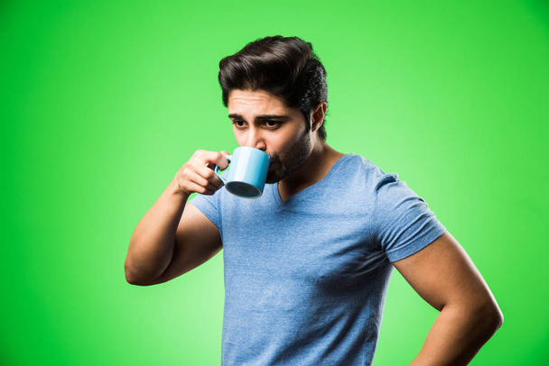 Hombre indio con taza de té / café o taza. Beber, presentar o sostener de pie aislado sobre fondo verde - Foto, Imagen