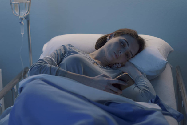 Sleepless patient lying in bed and chatting with her smartphone - Фото, изображение