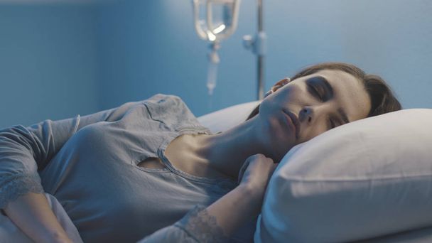Femme couchée dans le lit d'hôpital et dormant avec IV goutte à goutte
 - Photo, image