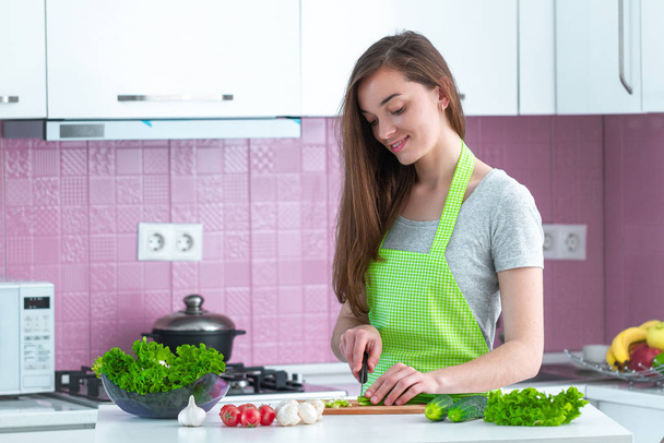 Mujer joven cocinera picando verduras para ensaladas frescas saludables y platos en la cocina en casa. Alimentos limpios y una nutrición adecuada. Preparación para la cena
  - Foto, Imagen