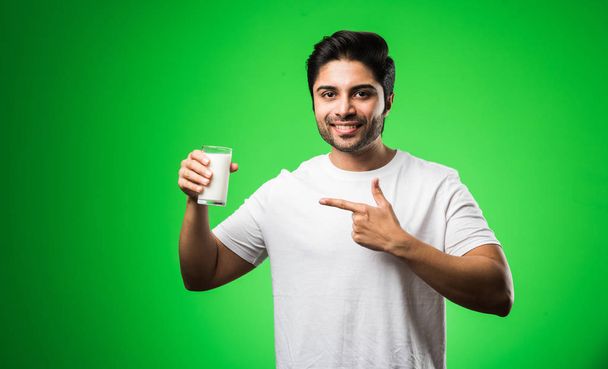 Ινδός άνθρωπος shwoing γάλα σε γυαλί, ενώ στέκεται απομονωμένο πάνω από το πράσινο φόντο - Φωτογραφία, εικόνα