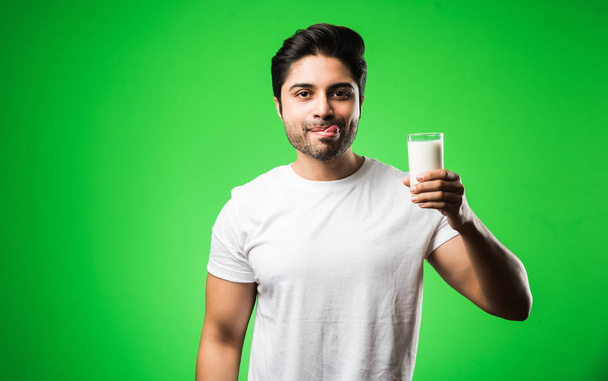 Indiase man shwoing melk in glas terwijl staan geïsoleerd over groene achtergrond - Foto, afbeelding