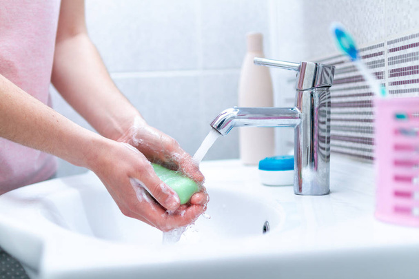 Mulher lavando as mãos com sabão sob a torneira com água no banheiro. Conceito de higiene e cuidados com as mãos
.  - Foto, Imagem