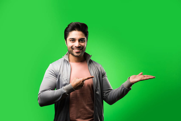 tevreden Indiase Man presenteren, wijzen, weergeven of adverteren met lege handen of vingers. staand geïsoleerd over groene achtergrond - Foto, afbeelding