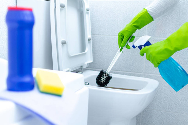 Huisvrouw in rubber handschoenen reinigen en ontsmetten toilet met behulp van schoonmaakmiddelen en een borstel. Schoonmaakdiensten  - Foto, afbeelding