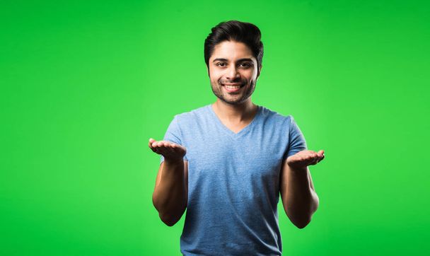 Tevreden indiaanse man die met lege handen of vingers presenteert, wijst, toont of adverteert terwijl hij geïsoleerd op een groene achtergrond staat - Foto, afbeelding