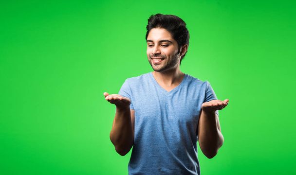 Satisfied indian man presenting, pointing, displaying or advertising with empty hands or fingers while standing isolated over green background - Photo, Image