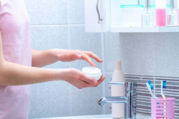 Using cream jar for dry skin in bathroom at home. Applying moisturizing and nourishing body cream. Skin care and nutrition - Φωτογραφία, εικόνα
