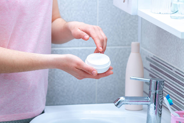 Using cream jar for dry skin in bathroom at home. Applying moisturizing and nourishing body cream. Skin care and nutrition - Zdjęcie, obraz