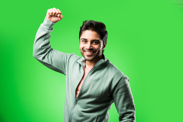 красивий індійський чоловік з успішним жестом, стоїть ізольовано на зеленому тлі - Фото, зображення