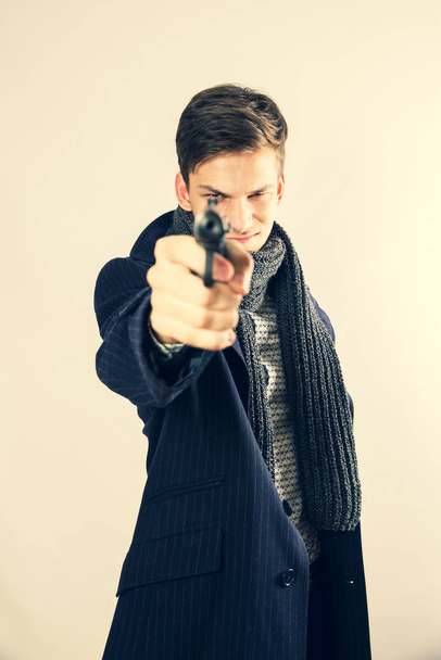 young man criminal aiming with gun over light background. Selective focus. - Фото, изображение