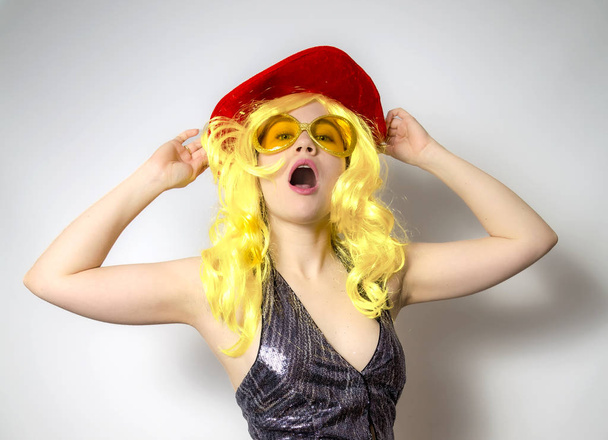 Portrait of an attractive young girl in a yellow wig wearing shiny clothes standing isolated over gray background, screaming - Fotografie, Obrázek