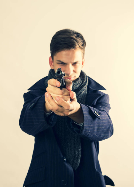 young man criminal aiming with gun over light background. Selective focus. - Фото, зображення