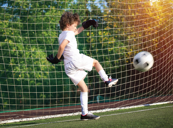 .Children's soccer football - a match of young children on the football field. Young goalie. Kids - soccer champion. Boy goalkeeper in football sportswear on stadium with ball. Sport concept. - 写真・画像